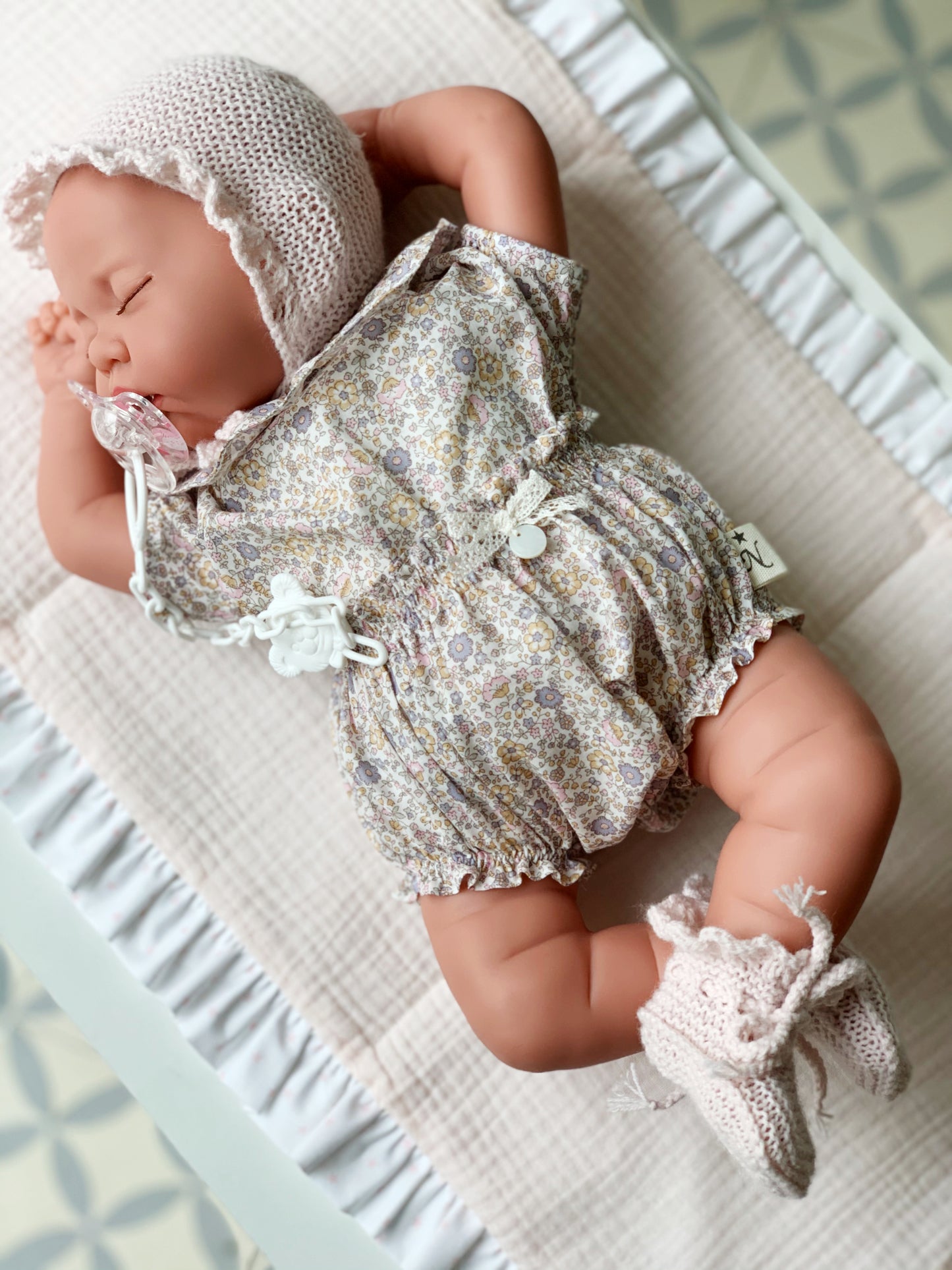 Reborn Luna, de 42 centímetros, vestida con capota y patucos botita, hechos a mano y blusa con cuello y manga corta a juego con el culotte. Incluye chupete.